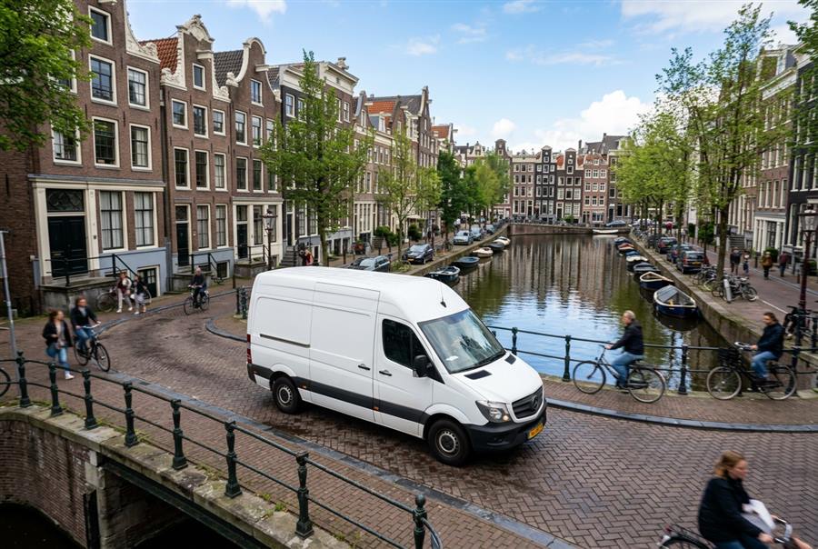 Witte bestelbus rijdt door een historische Nederlandse binnenstad