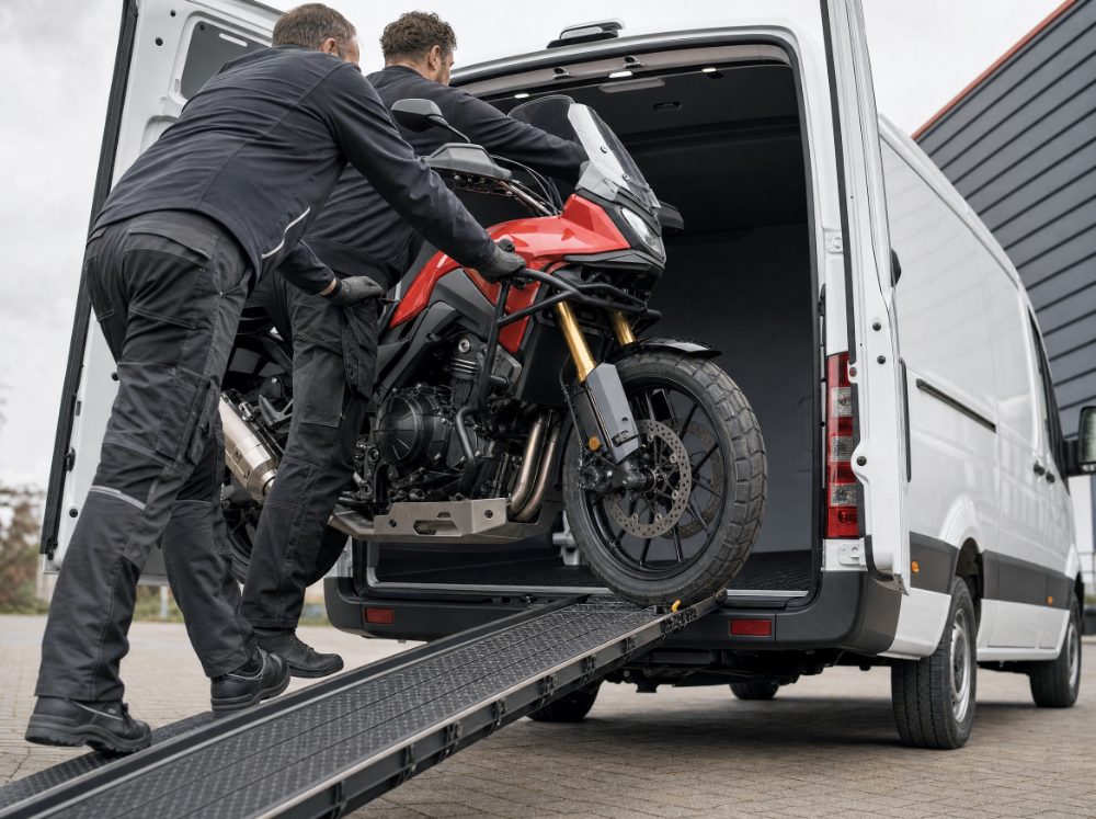 Twee mannen duwen een motor over de oprijplaat de Sprinter in
